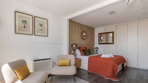 Une chambre à coucher comprenant un lit, deux chaises, un radiateur, un miroir et deux reproductions botaniques encadrées accrochées au mur.