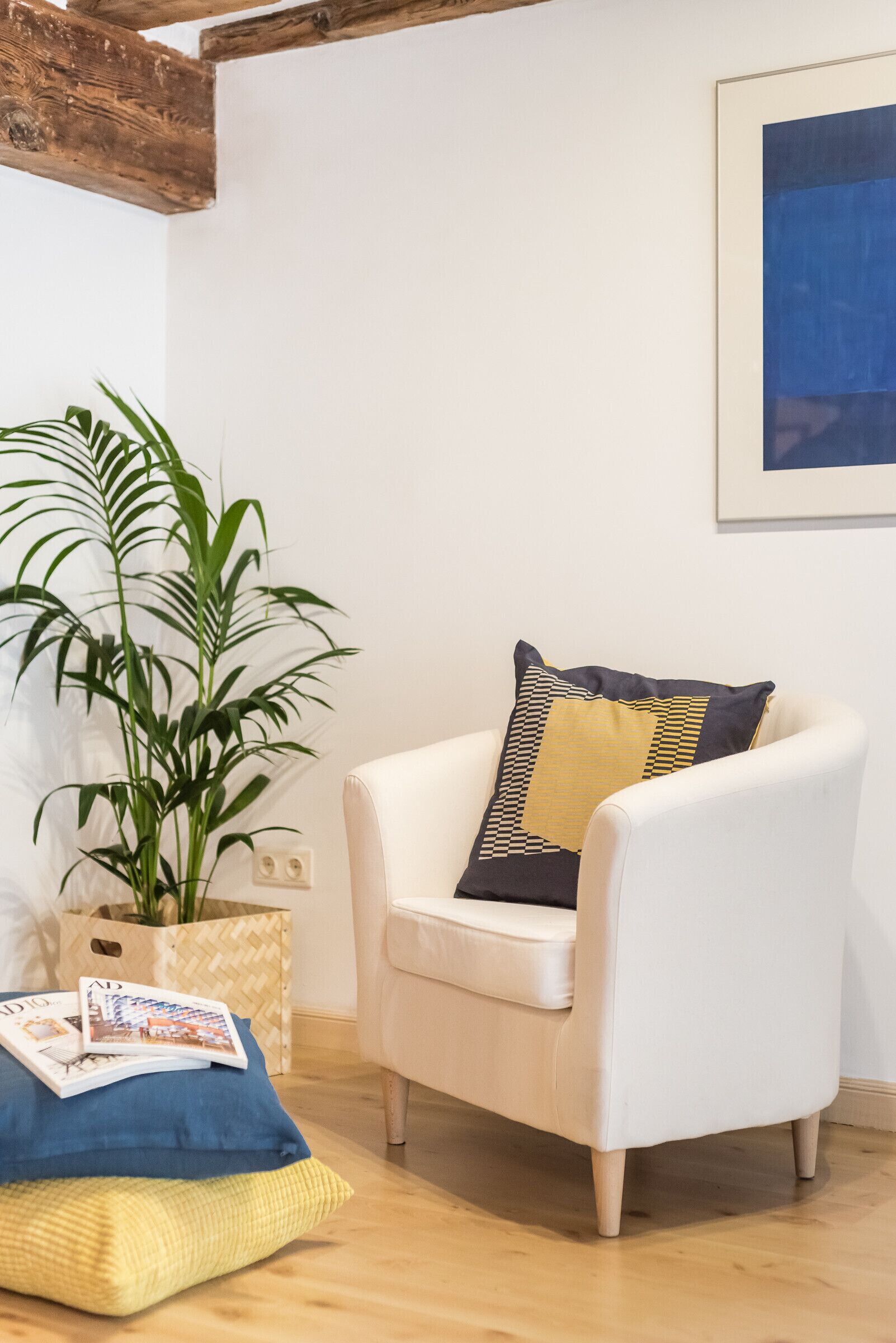 A white armchair with a patterned cushion, a potted plant, and a framed picture on the wall.
