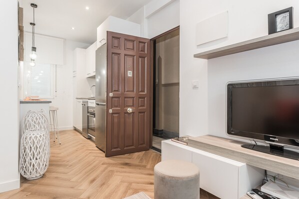 Una cocina moderna con suelo de madera, una puerta grande color café y un televisor de pantalla plana sobre un atril de madera.