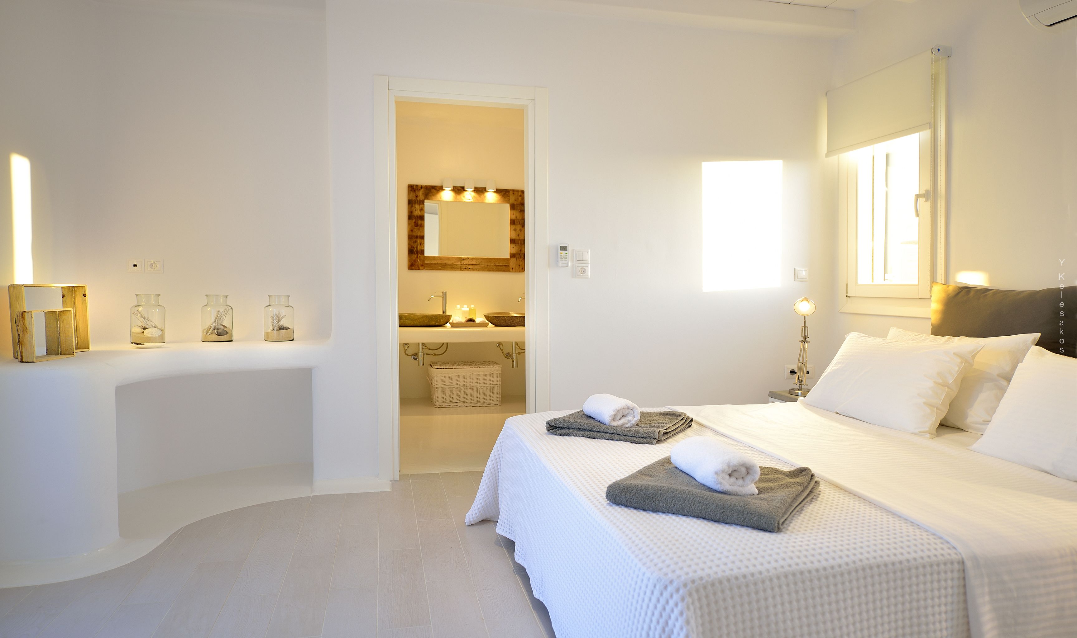 A hotel room with a large bed, a bathroom with a sink and mirror, and a view of the sea.