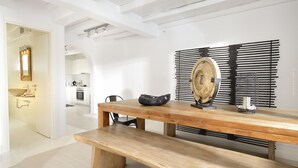 A modern kitchen with white cabinetry, a wooden dining table with benches, and a decorative wall piece. - Villa Blanca Uno (Mykonos)
