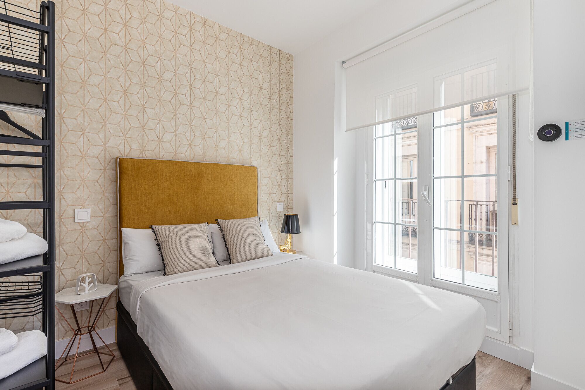 Ein Hotelzimmer mit Bett, Nachttisch, Lampe, Fenster mit Blick und Handtuchhalter.