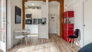 Een moderne keuken met roestvrijstalen apparatuur, een eethoek met een transparante tafel en metalen stoelen, en een rode schapunit.