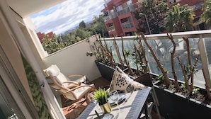 Un balcón con mesa lista para dos personas, sillas y plantas en macetas.