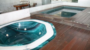 Un área de spa con un jacuzzi y una piscina más pequeña, suelo de madera y una pared de vidrio.