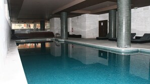 Una piscina interior con agua cristalina, sillas de descanso y suelo de baldosas.