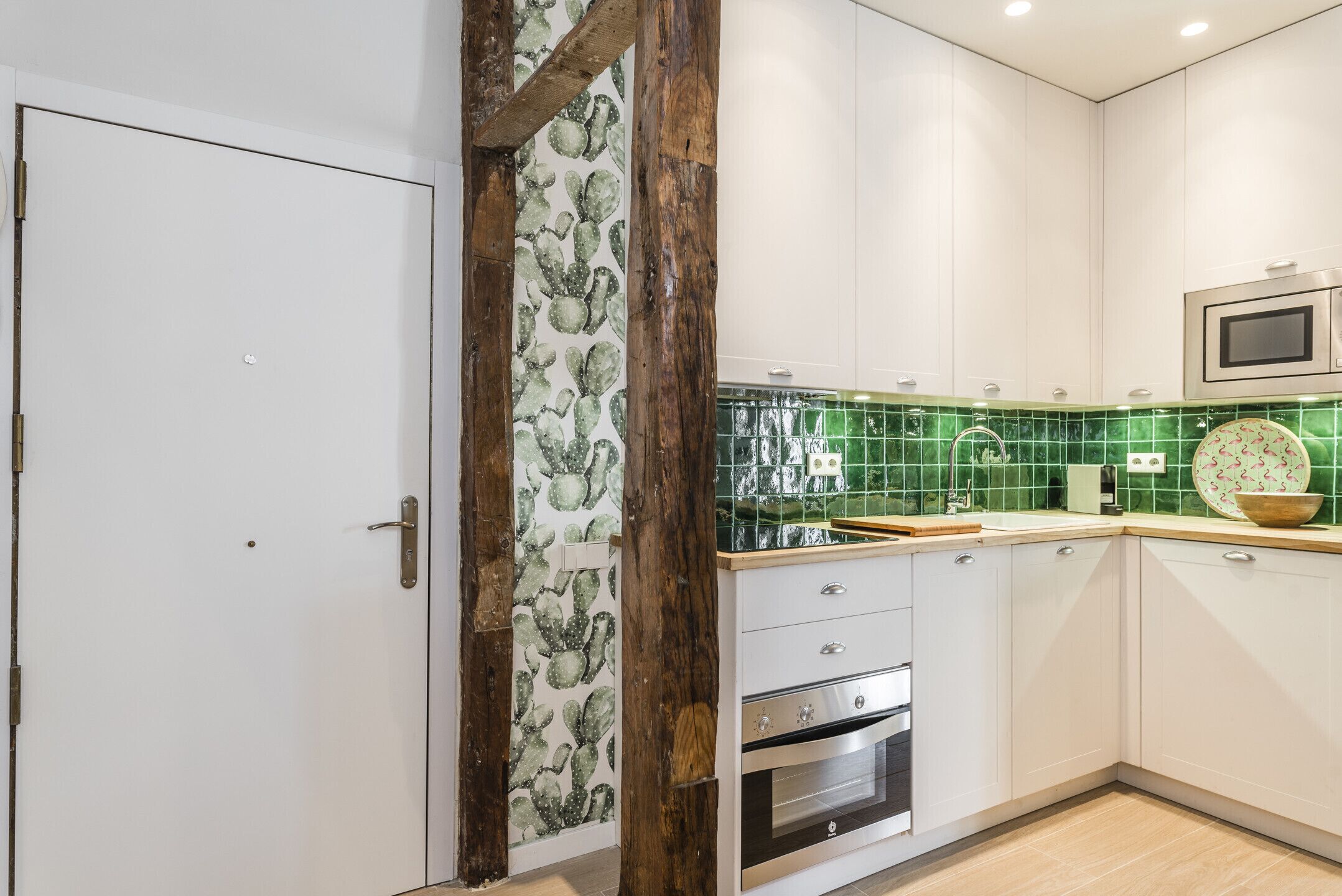 Cozinha com armários brancos, painel de azulejos verdes e uma viga de madeira.