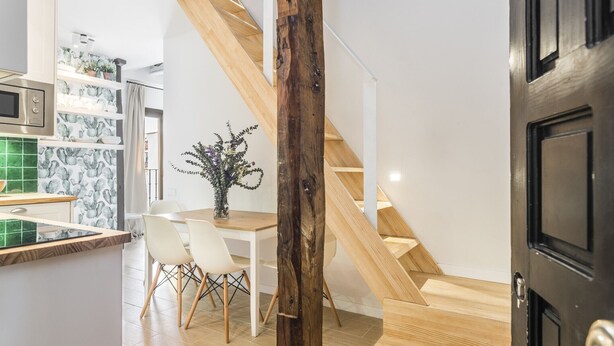 A modern kitchen with white cabinets, a wooden staircase, and a dining area with a white table and chairs. - Waou Sol III - Alquiler de Corta Duración (Madrid)