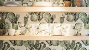 A kitchen with a cactus-themed wallpaper, wooden shelves, and various kitchenware. - Waou Sol III - Alquiler de Corta Duración (Madrid)