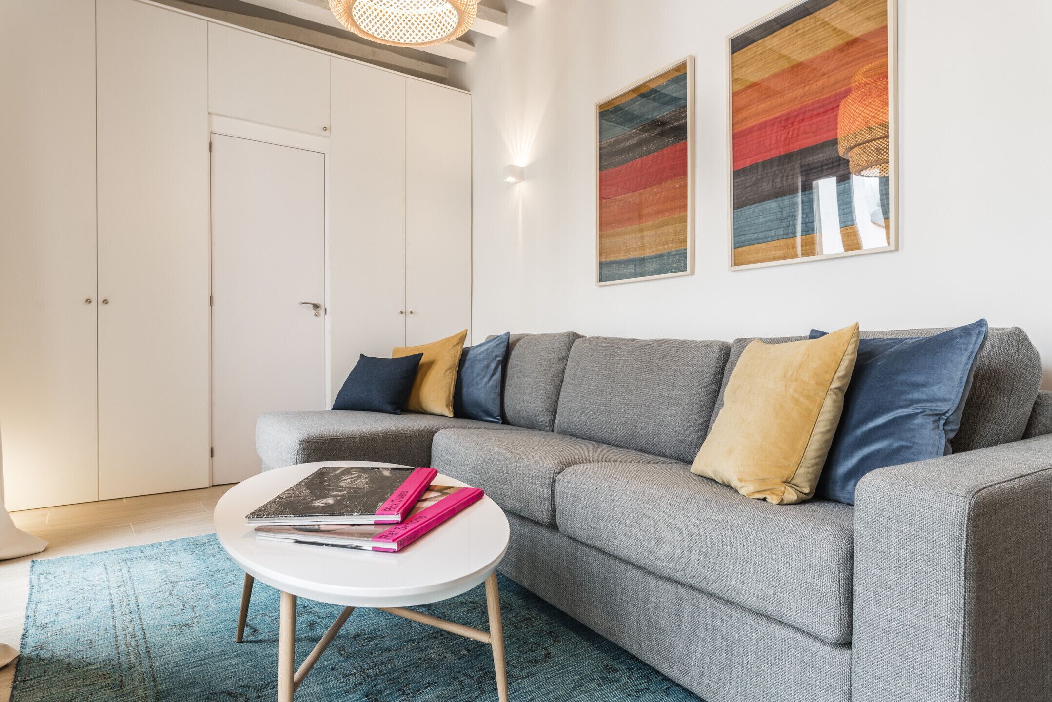 Een moderne woonkamer met een grijze bank, een ronde witte salontafel en een blauw vloerkleed.