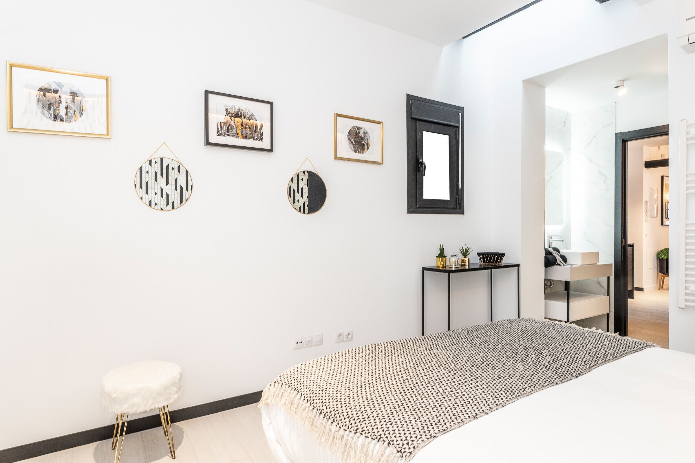 A modern bedroom with a bed, a small stool, a side table, and wall art.