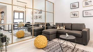 A modern living room with a sectional sofa, a round yellow pouf, a small coffee table, and framed pictures on the wall. - Waou Malasaña es MIA - Corta Duración (Madrid)