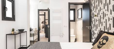 A modern bedroom with a bed, a console table, a patterned rug, a geometric wall design, and a door leading to another room.