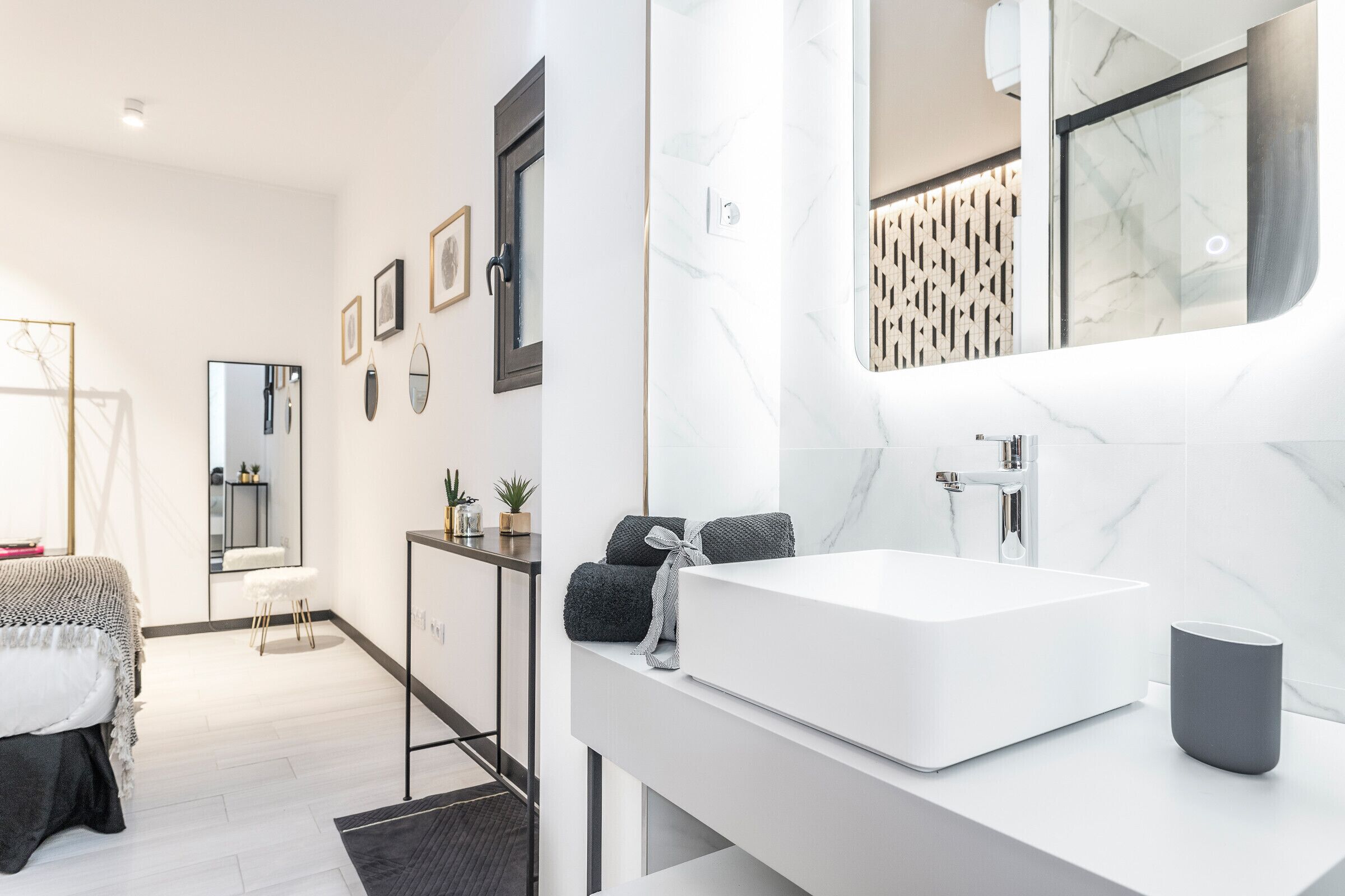 Une salle de bain moderne avec un grand miroir, un lavabo blanc et un porte-serviettes.