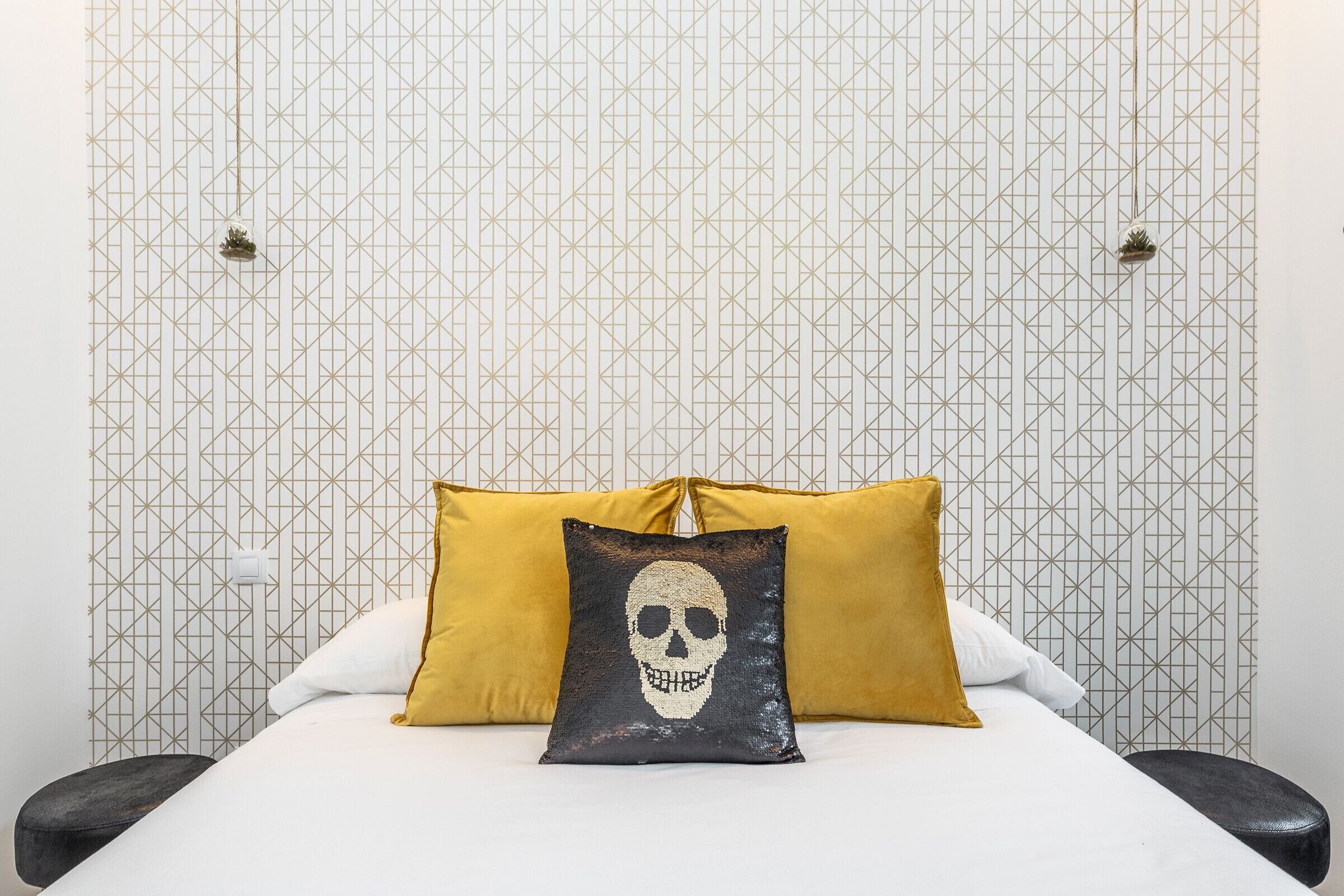 A bed with two pillows, one with a skull design, and a patterned wall.