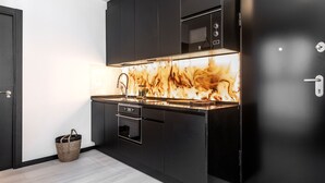 A modern kitchen with dark cabinetry, a stainless steel microwave, and a unique backsplash with a fiery design. - Waou Malasaña es MIA - Corta Duración (Madrid)