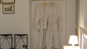 Ein Hotelzimmer mit zwei schwarzen Stühlen, einem weißen Bett und zwei weißen Bademänteln, die an der Wand hängen.