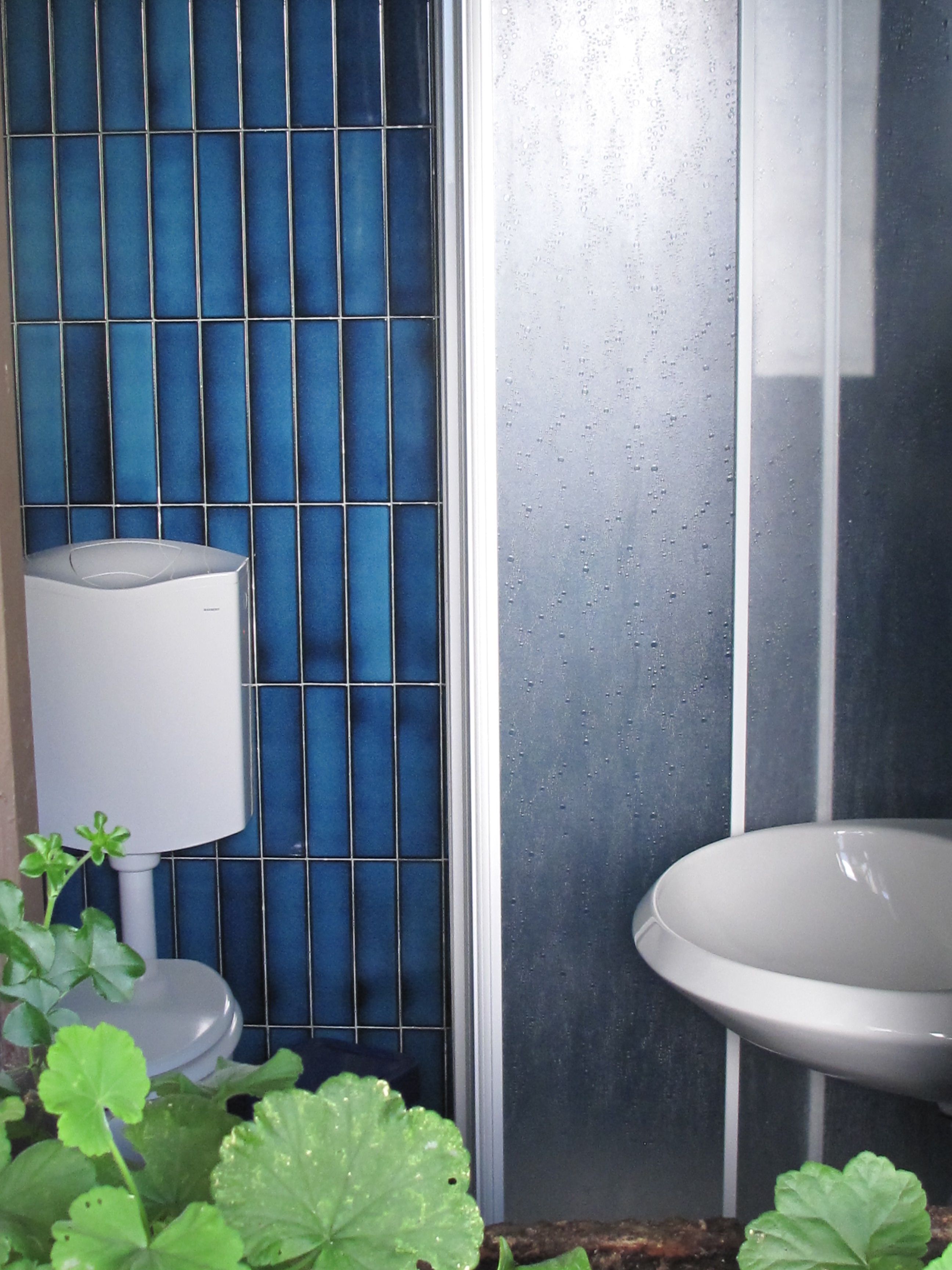 A bathroom with a blue tiled wall, a white sink, and a white toilet.