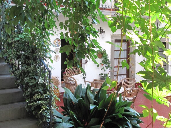 Un espacio al aire libre techado con mobiliario de mimbre, plantas en macetas y una escalera.