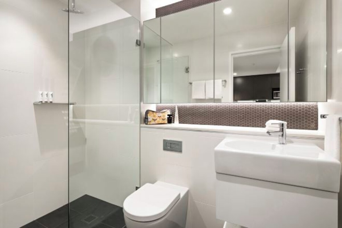 A modern bathroom with a glass shower enclosure, a white toilet, and a sink with a mirror above it.