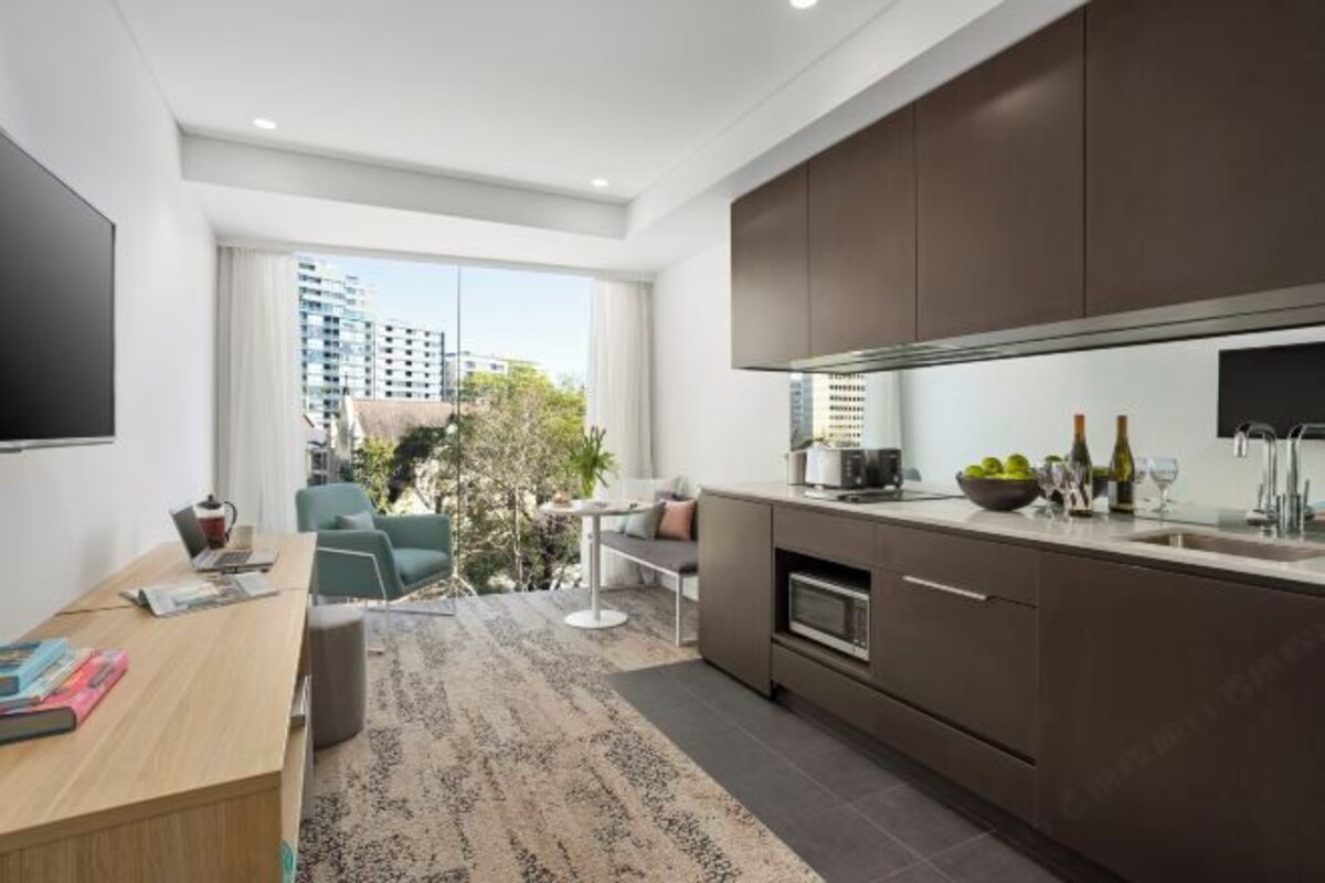 A modern kitchen with dark cabinets, a built-in oven, and a large window offering a city view.