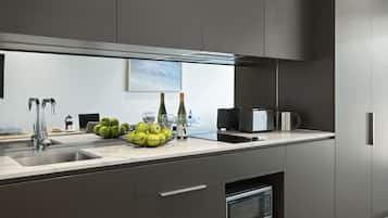 A modern kitchen with a stainless steel sink, a bowl of green apples, wine bottles, glasses, and a coffee maker.