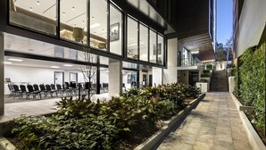 A modern building with large windows, a seating area with chairs, and a staircase leading to an upper level. - Quest North Sydney (North Sydney)