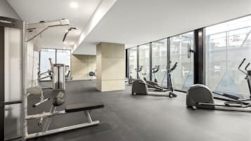 A modern gym with various exercise equipment, large windows, and a clean, minimalist design.
