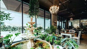A spacious indoor area with a central fountain surrounded by various potted plants. There are dining tables and chairs in the background, suggesting a dining or lounge area. - Quest North Sydney (North Sydney)