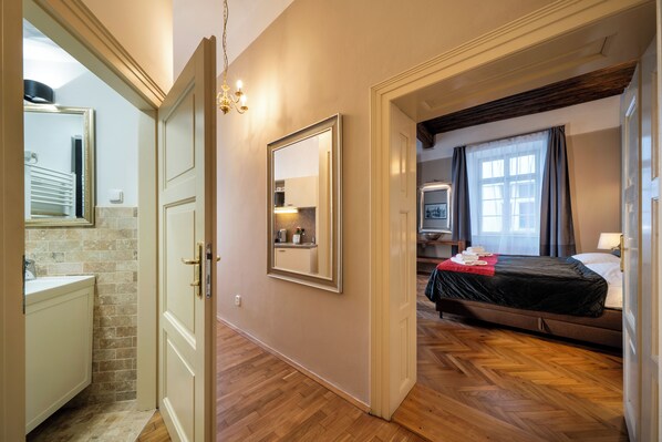 Ein Hotelzimmer mit Holzboden, einem Bett mit schwarzer Bettdecke, einem großen Spiegel und Blick in die Küche durch eine offene Tür.