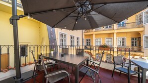 Een terras buiten met een tafel, stoelen, een grote parasol en een hekwerk.