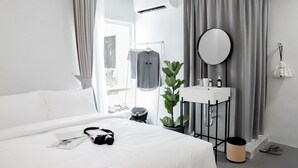 Habitación de hotel moderna con cama, mesita de noche con espejo, lavamanos pequeño y planta en maceta.