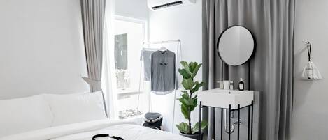 A modern hotel room with a bed, a bedside table with a mirror, a small sink, and a potted plant.