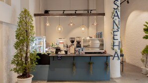 Un café con mostrador azul, lámparas colgantes y una máquina de café, con un letrero que dice "SANEHA".