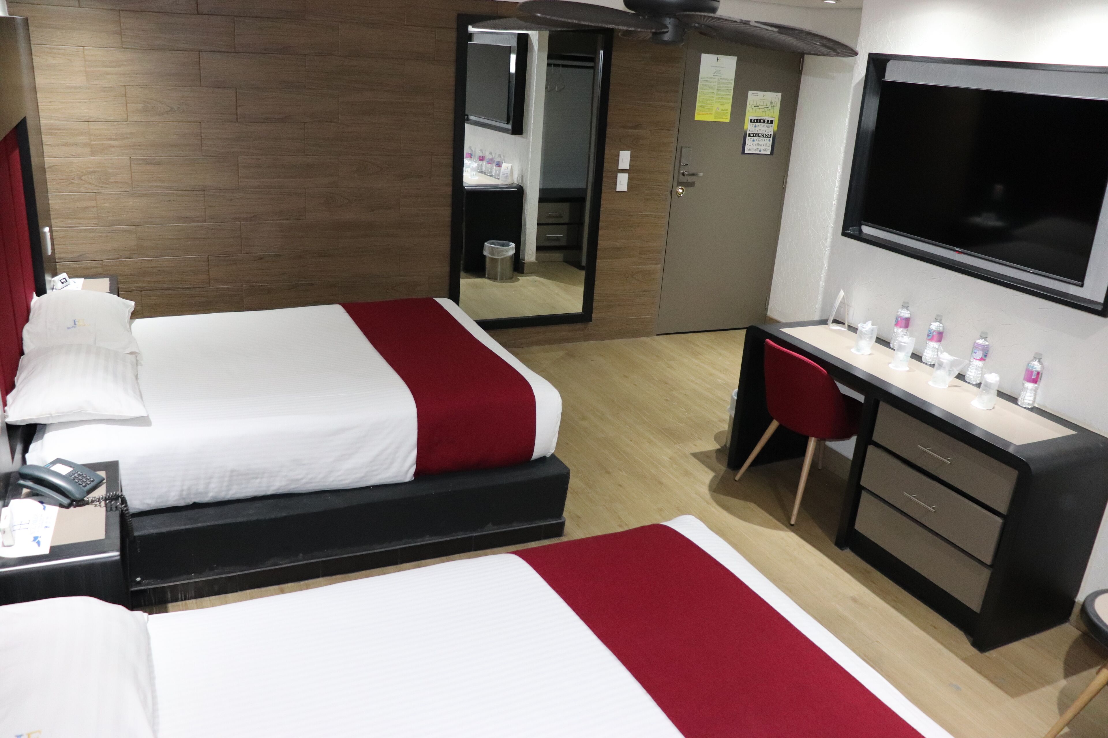 Habitación de hotel con cama, escritorio, espejo, televisor y armario.