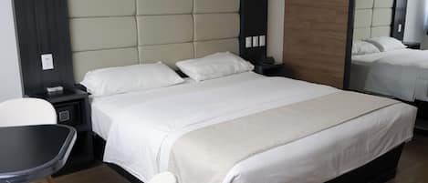 A hotel room with a large bed, a bedside table, a chair, and a mirror.