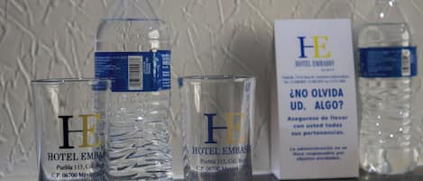 Three clear glasses and two water bottles with labels on a table.