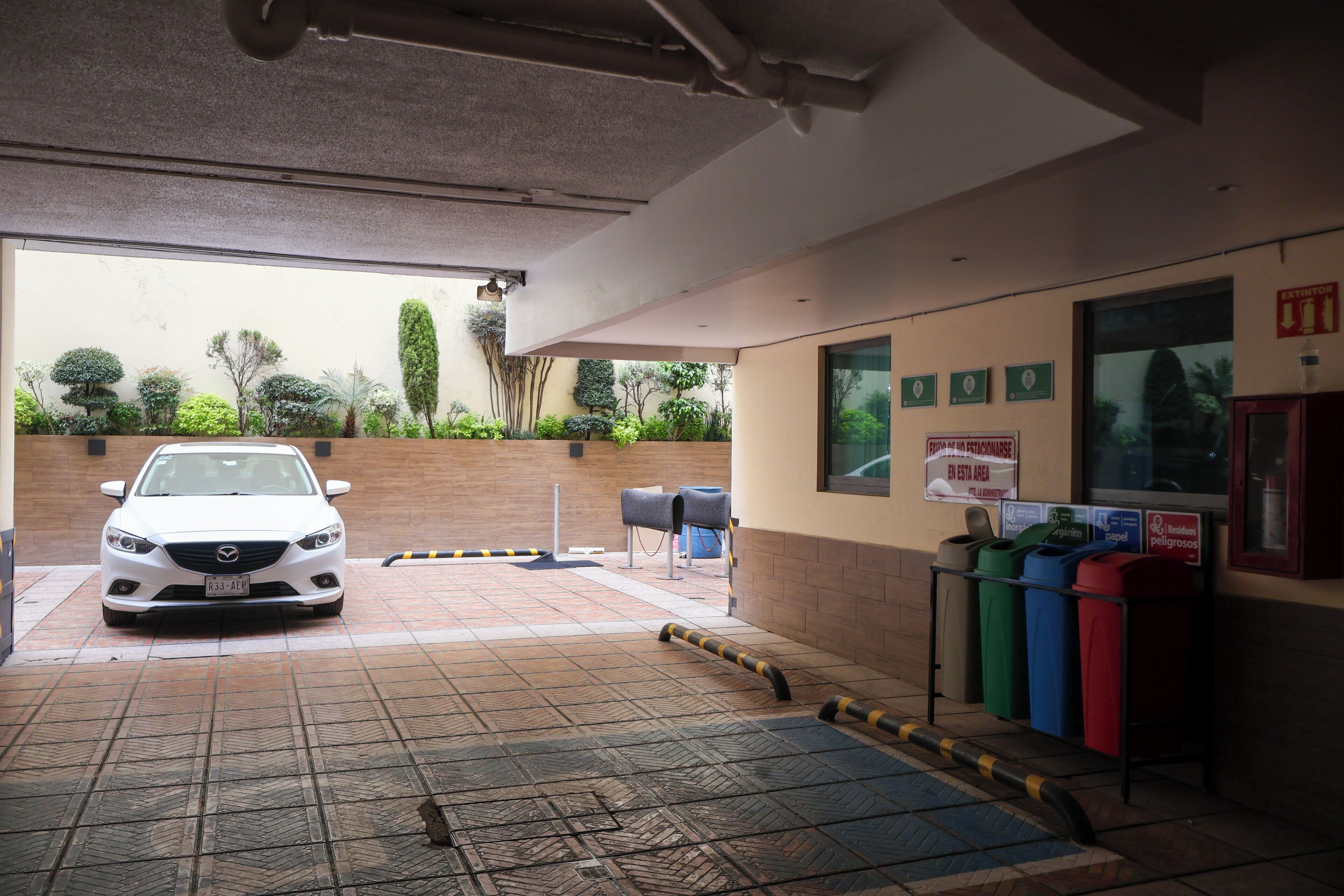 A parking area with a white car, a trash bin, and a recycling bin.