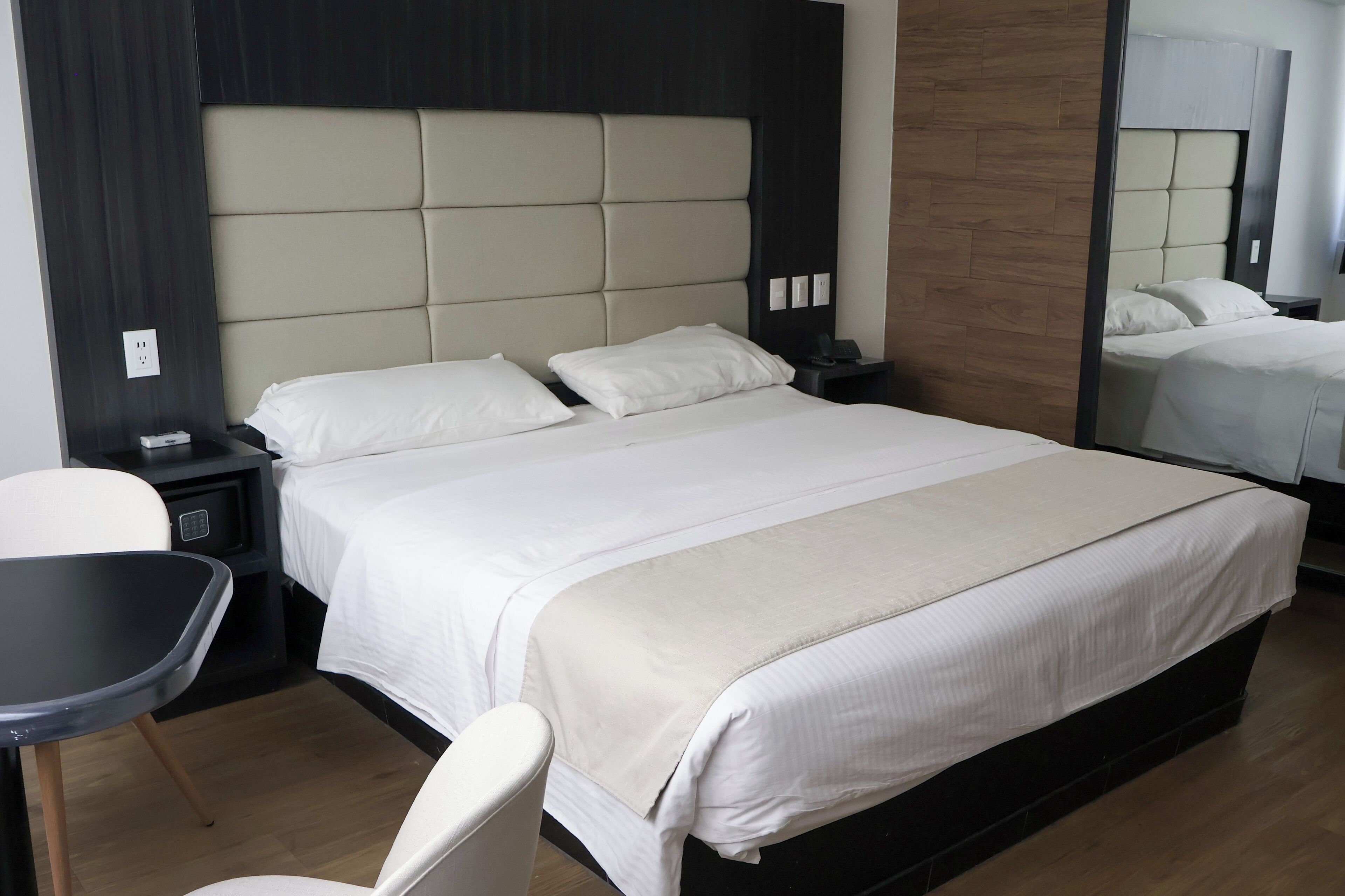 A hotel room with a large bed, two bedside tables, a chair, and a mirror.