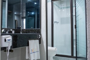 Un baño con cabina de ducha de vidrio, inodoro blanco, lavabo con espejo y una toalla colgada en la pared.