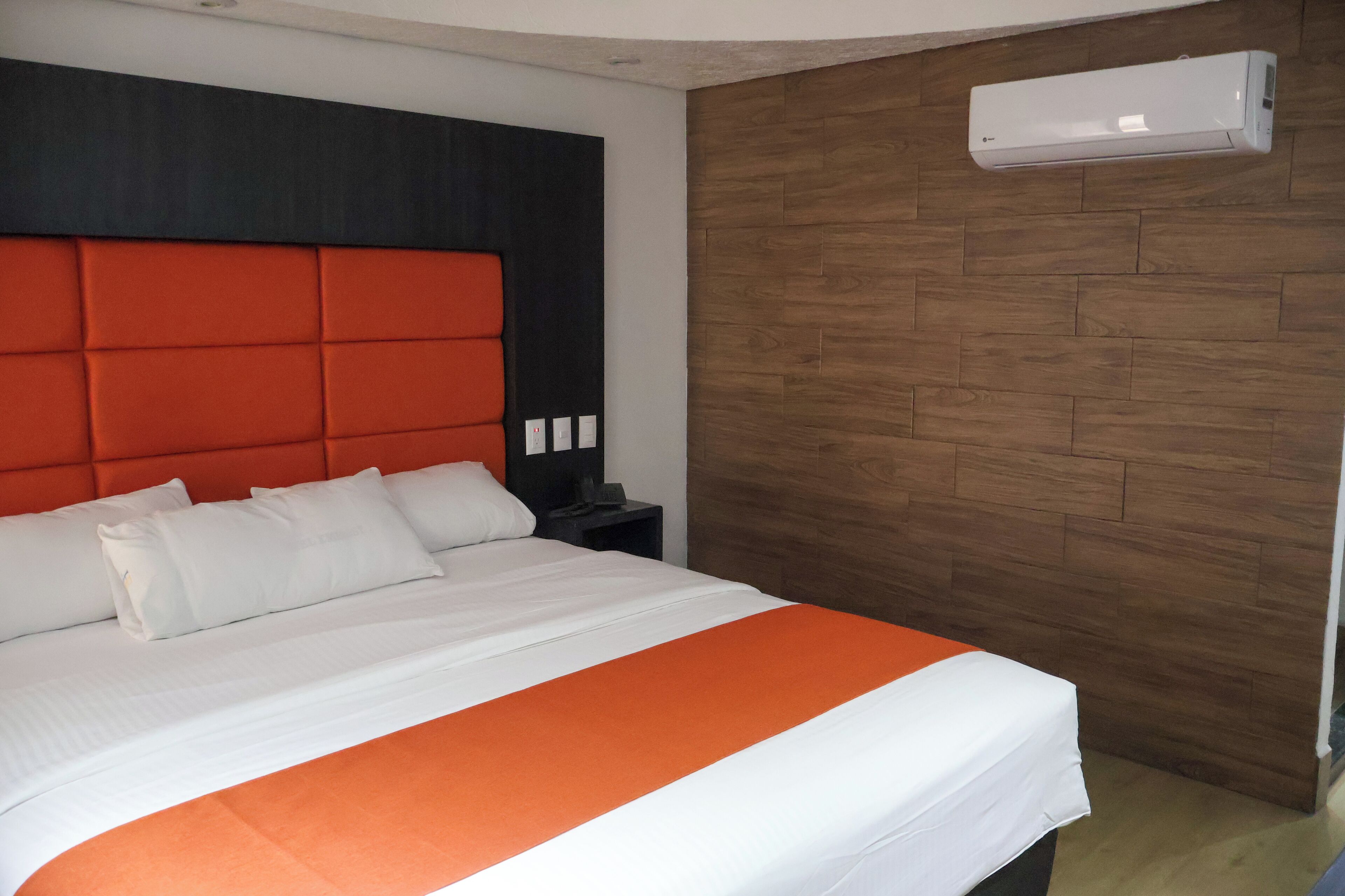 Una habitación de hotel moderna con una cama grande, una pared de acento de madera y un equipo de aire acondicionado.