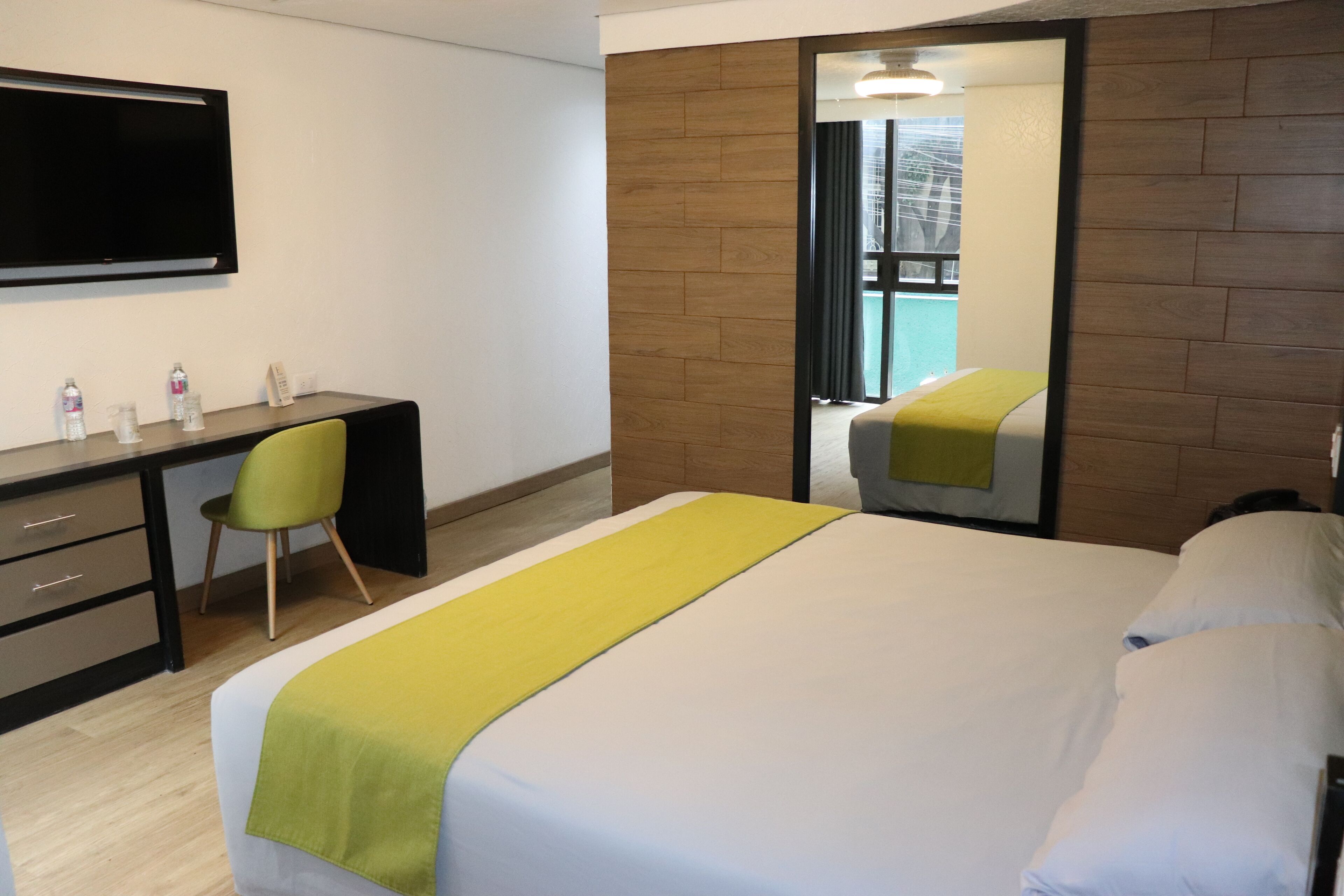 A hotel room with a bed, a desk with a chair, a flat-screen TV, and a mirror.