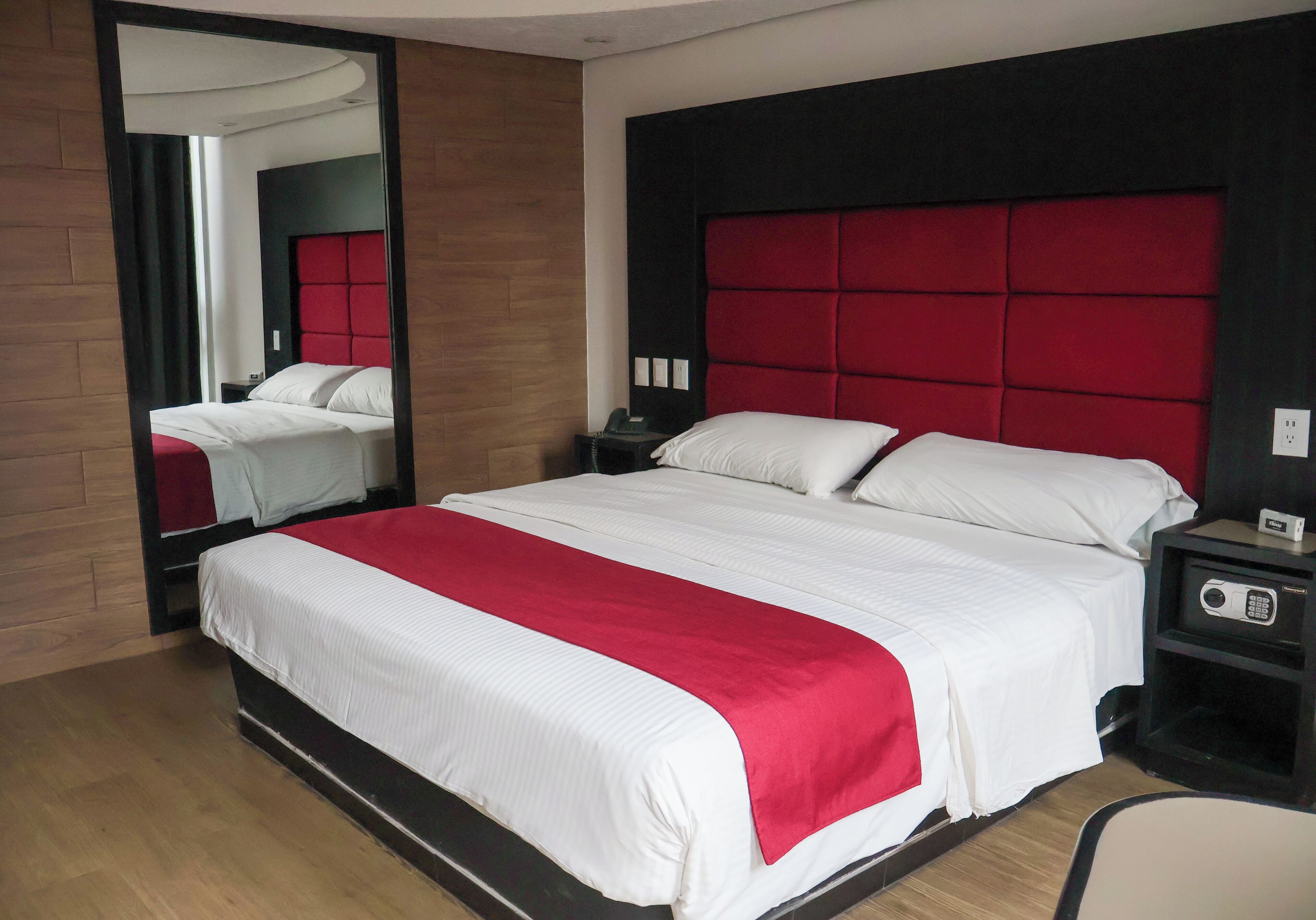 Habitación de hotel con una cama grande, un espejo, una mesita de noche y un cabecero rojo.