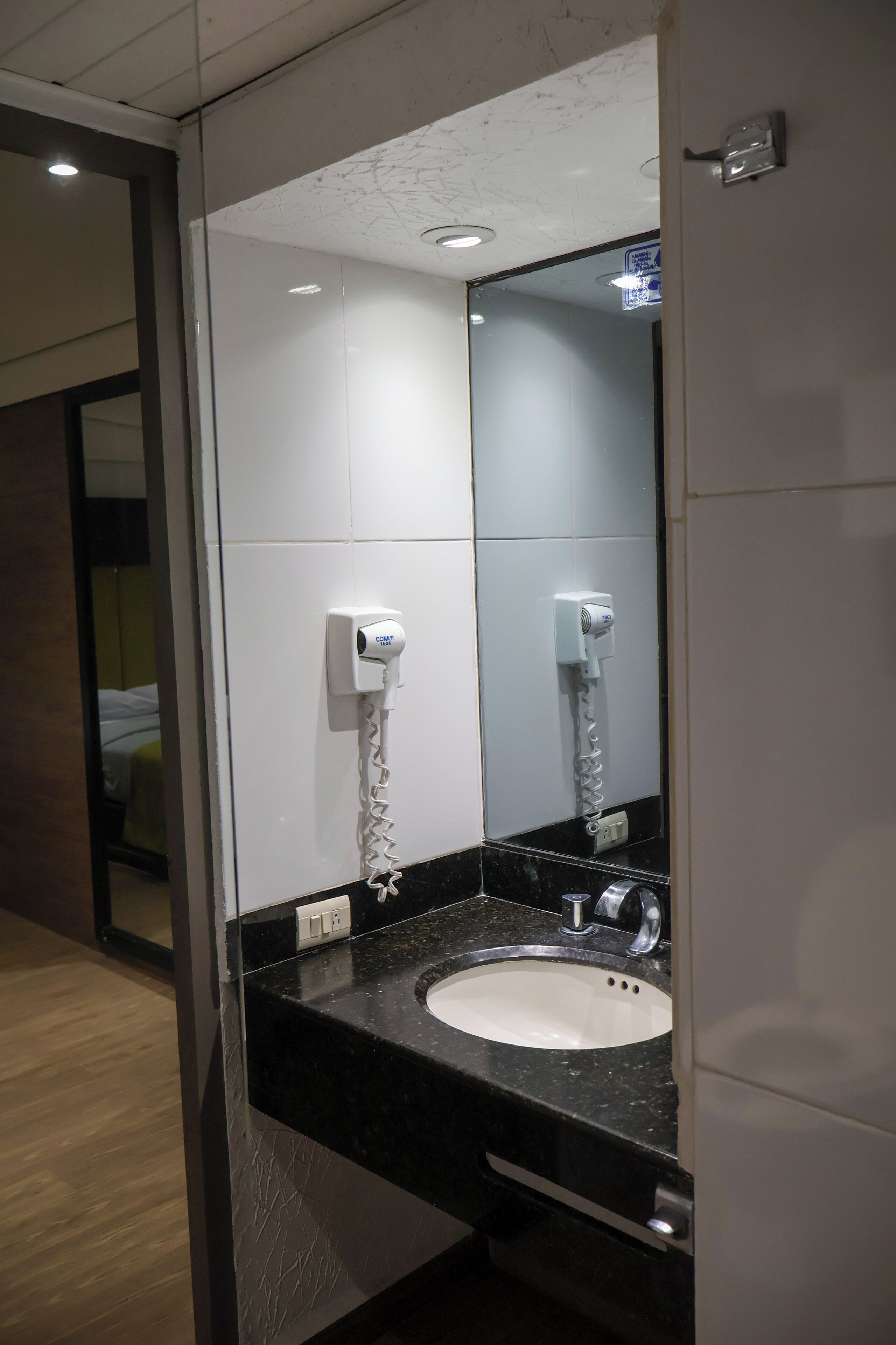 Un baño moderno con una encimera negra, un lavabo blanco y un secador de pelo fijado a la pared.