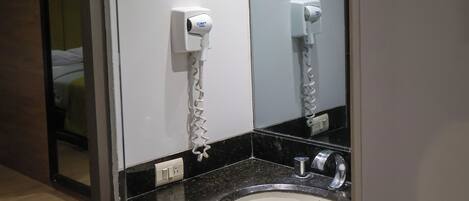 Un baño moderno con una encimera negra, un lavabo blanco y un secador de pelo fijado a la pared.