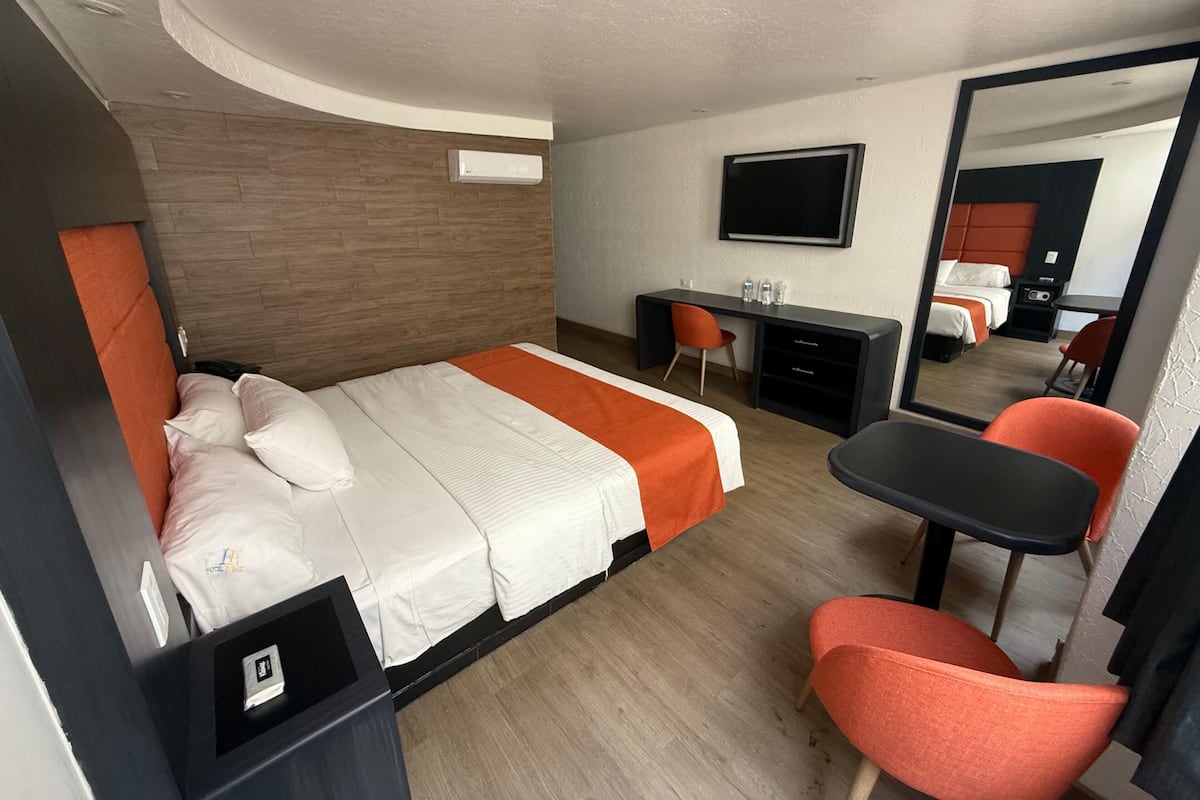 Habitación de hotel con cama, escritorio, sillas y televisor.