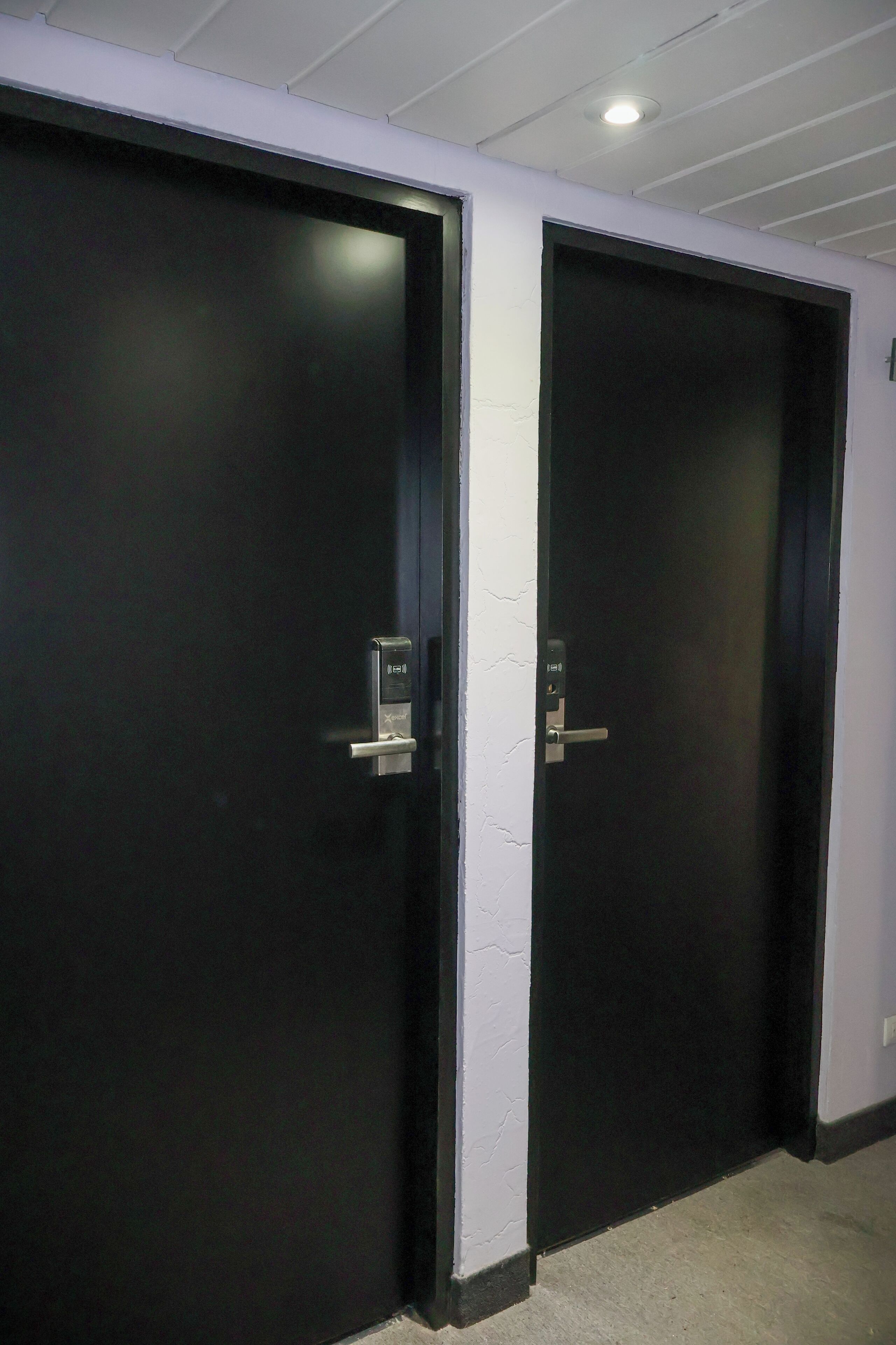 Zwei schwarze Türen mit Griff und Schloss, weiße Wände und eine Decke mit eingelassenen Leuchten.
