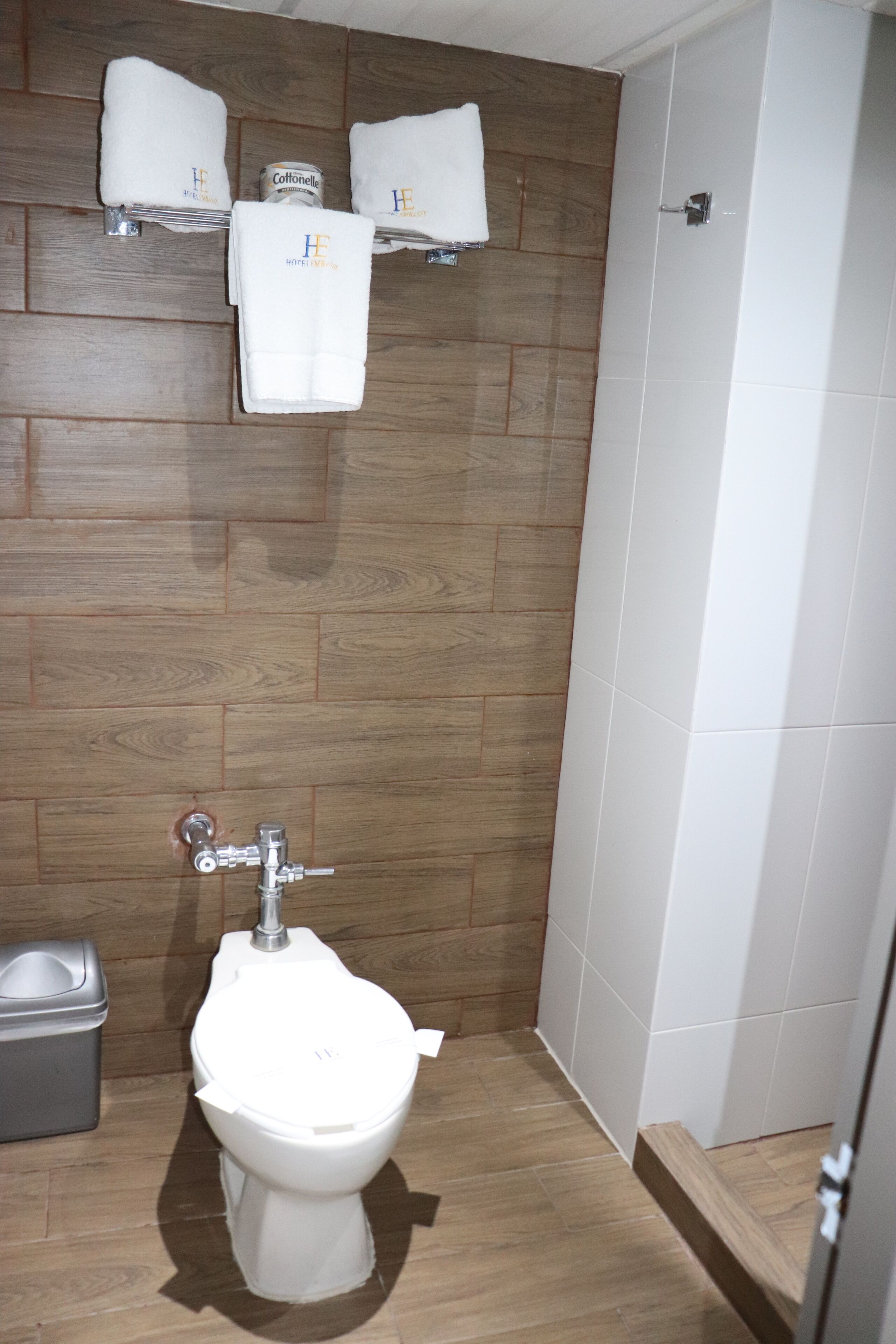 A bathroom with a wooden wall, a white toilet, and two towels on a shelf.