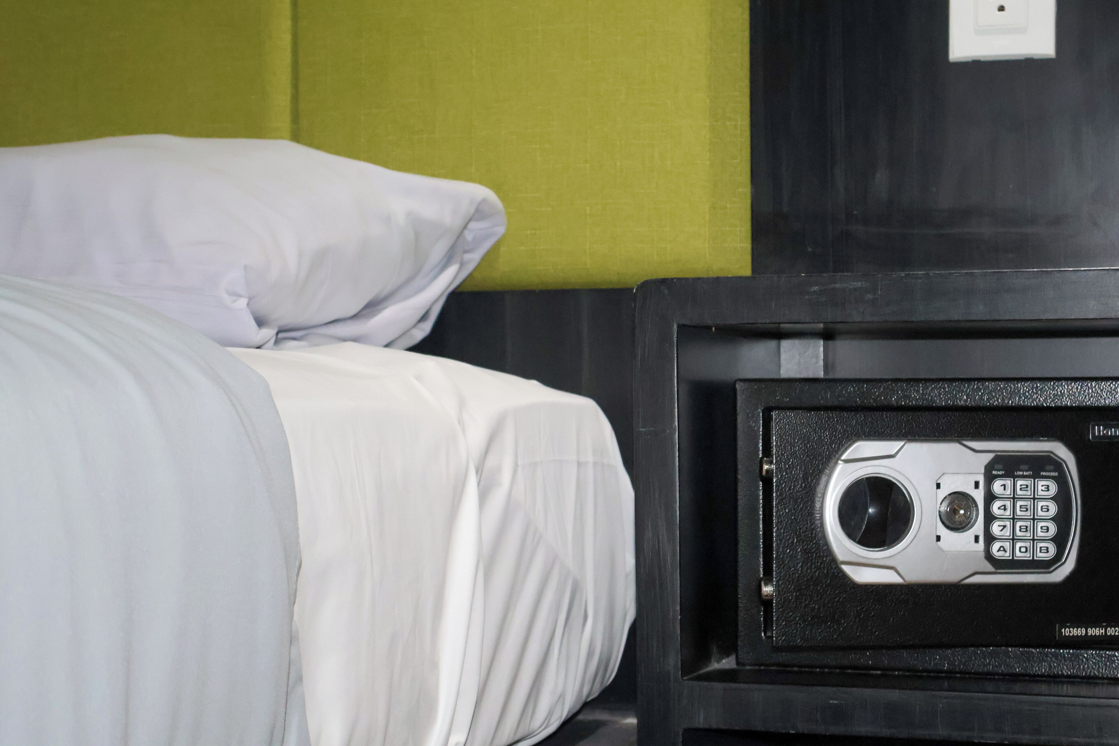 A bed with white bedding and a black headboard, a nightstand with a built-in safe, and a green wall.