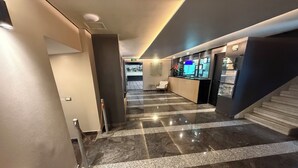 A hotel lobby with a marble floor, a reception desk, a staircase, and a seating area.